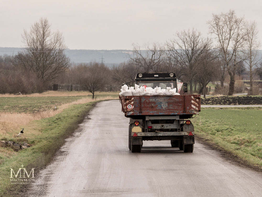 A tractor drives a flatbed with white sacks. Photograph created with the Olympus M. Zuiko digital ED 40 - 150 mm 1:2.8 PRO.